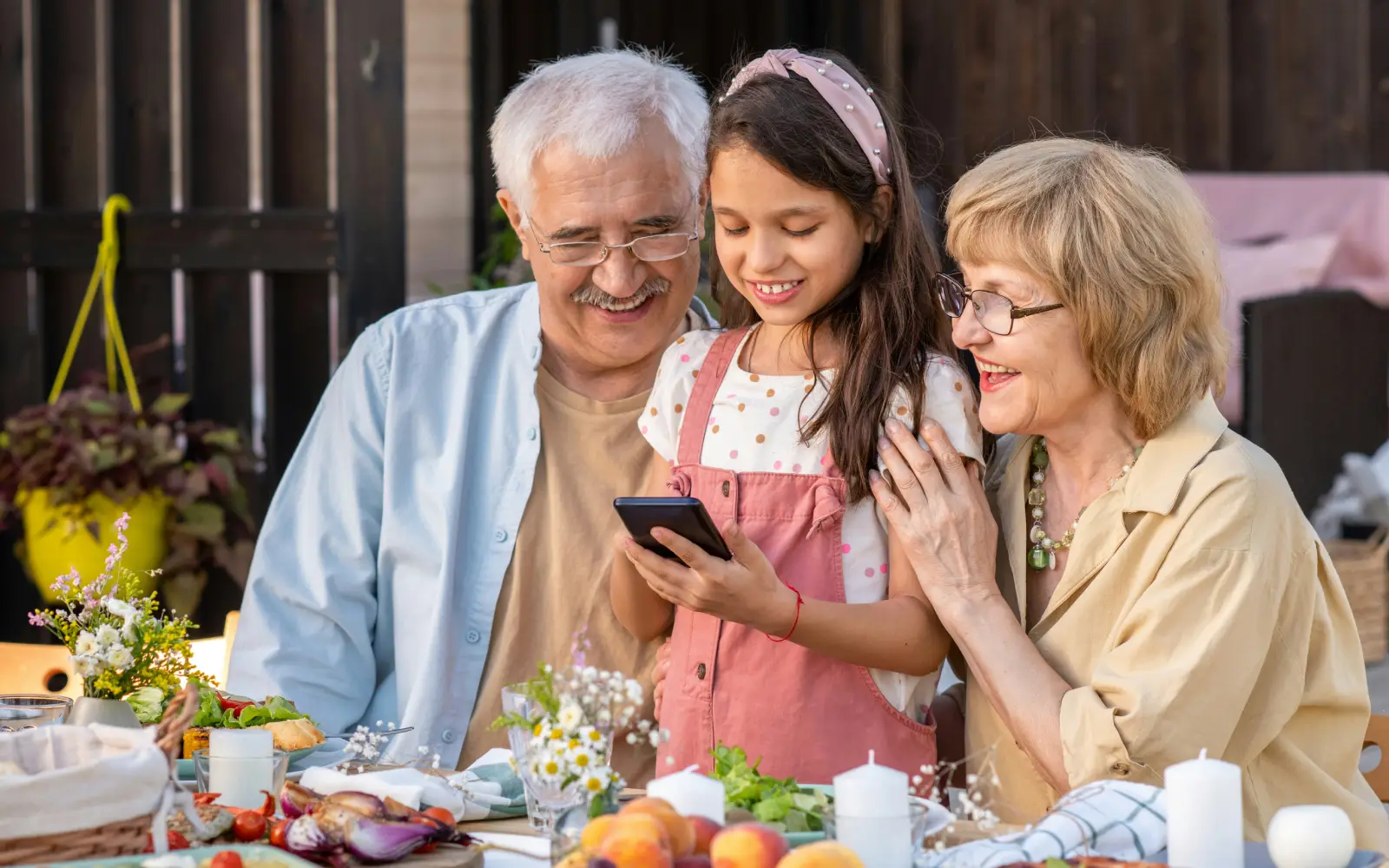 Grandparents and granddaughter smiling at a phone together at family meal